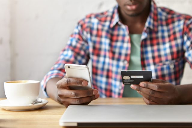 Close up shot of male hands holos mug debit cad and mobile phone, entering data for web-site form, going to pay for online order. People, lifestyle, modern technologies and e-commerce concept